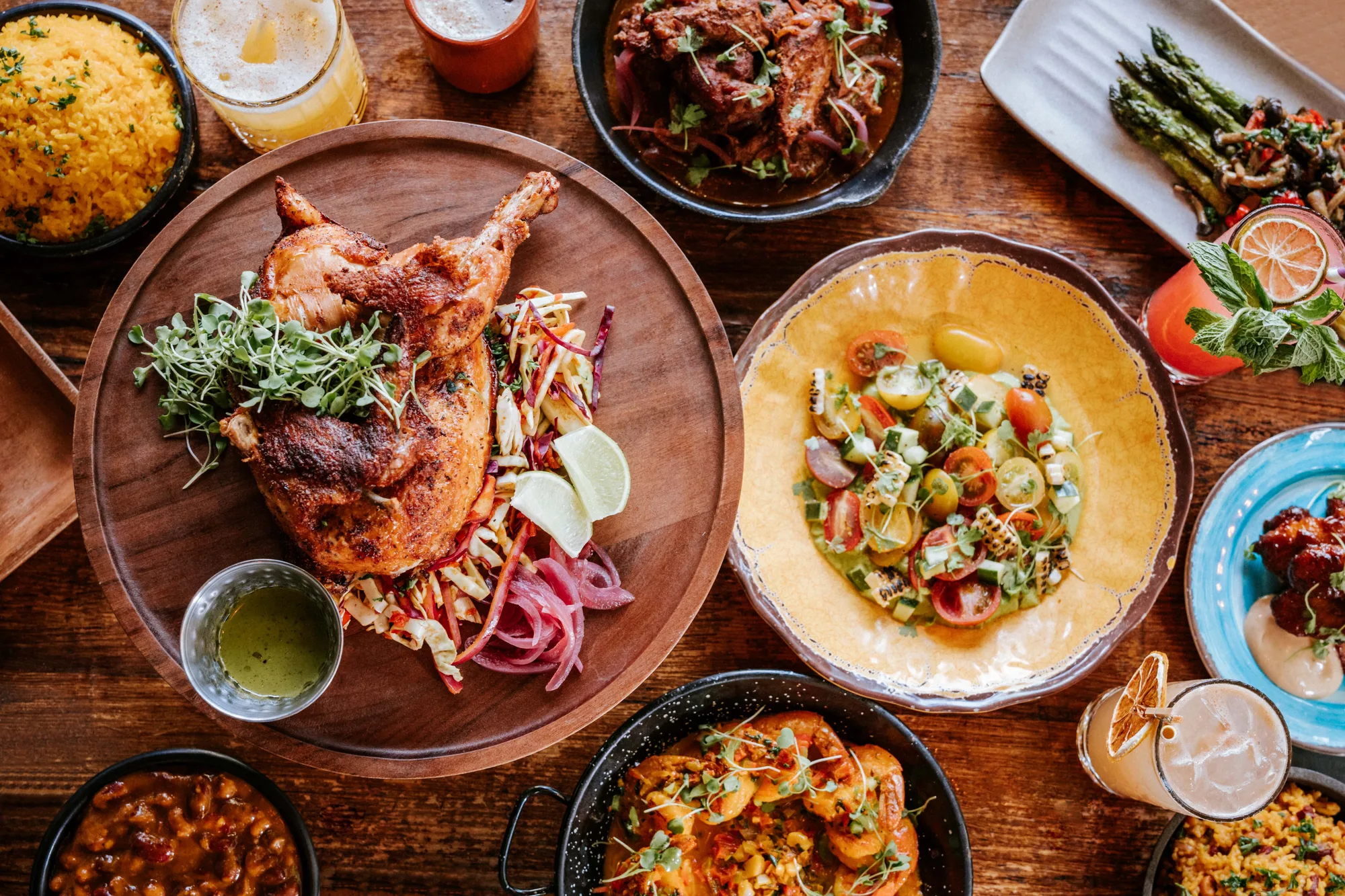 Overhead spread of roasted chicken, rice, vegetables, and drinks at alaMar