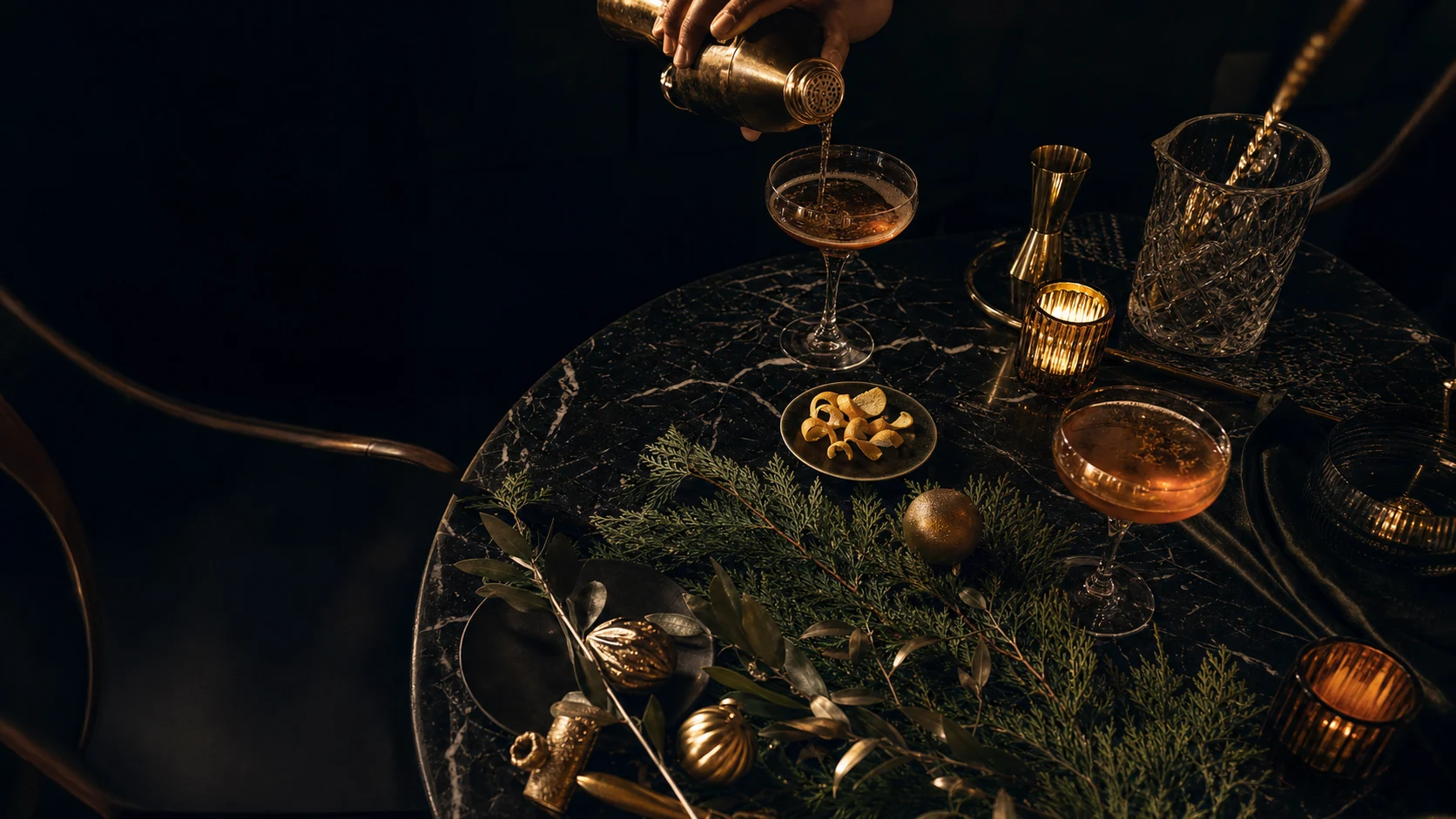 Festive holiday cocktail table with greenery, candlelight, and a drink being poured