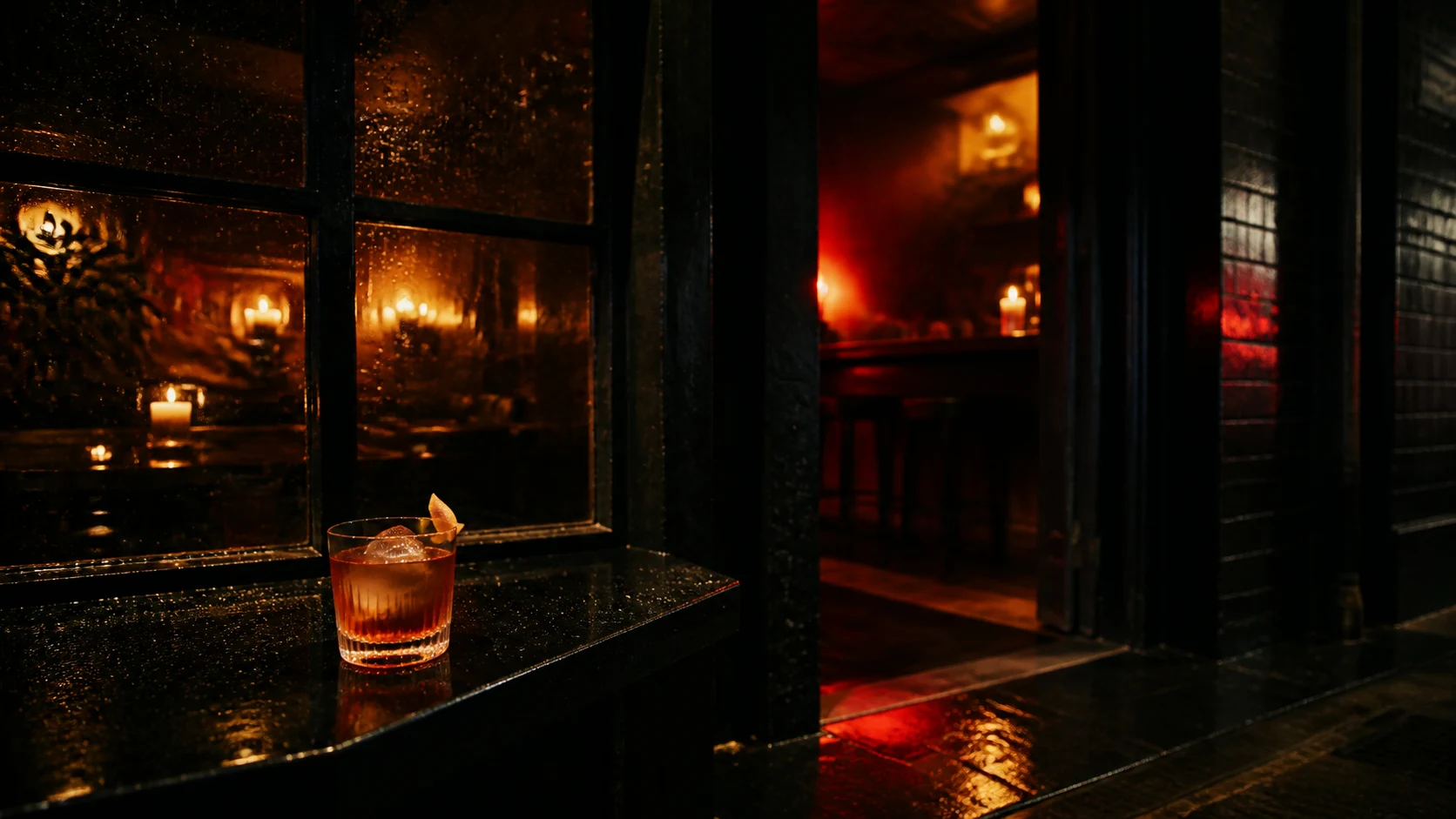 Rainy after-dark restaurant window with amber light and a cocktail on a ledge